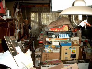 An untidy room filled with personal belonging piled up on the floor and surrounding furniture