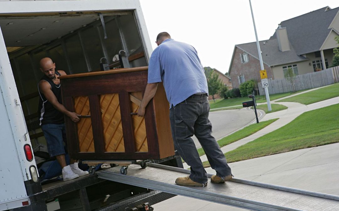 A couple of removals people carefully unloading a piano on a specialist wheeled sled and ramp