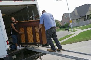 A couple of removals people carefully unloading a piano on a specialist wheeled sled and ramp