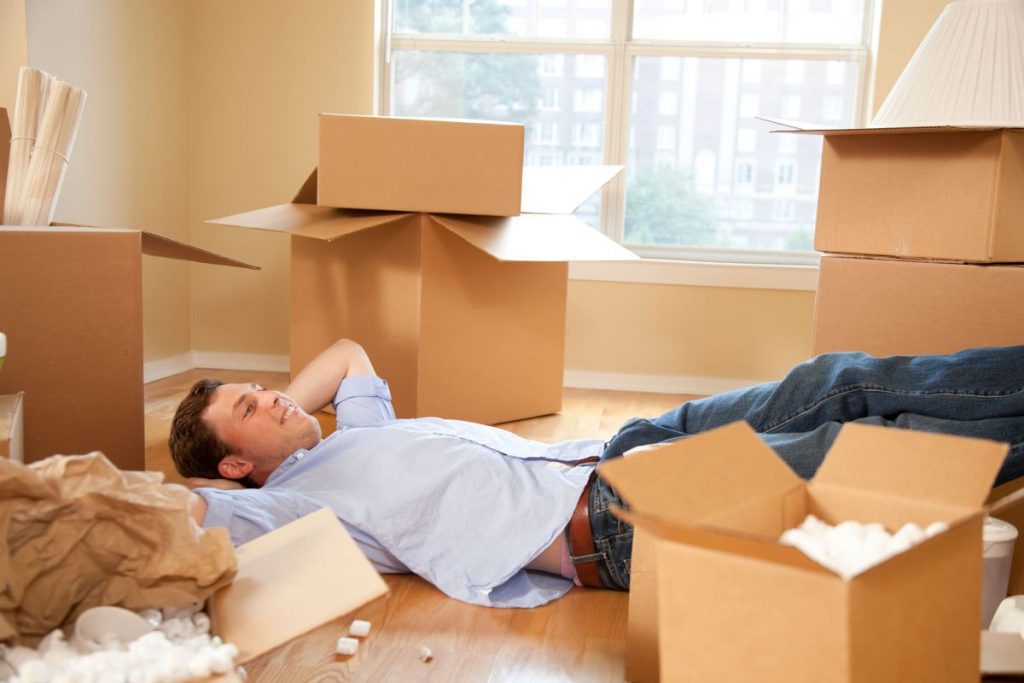 A happy man laying on the floor of his new flat surrounded by partially unpacked removals boxes