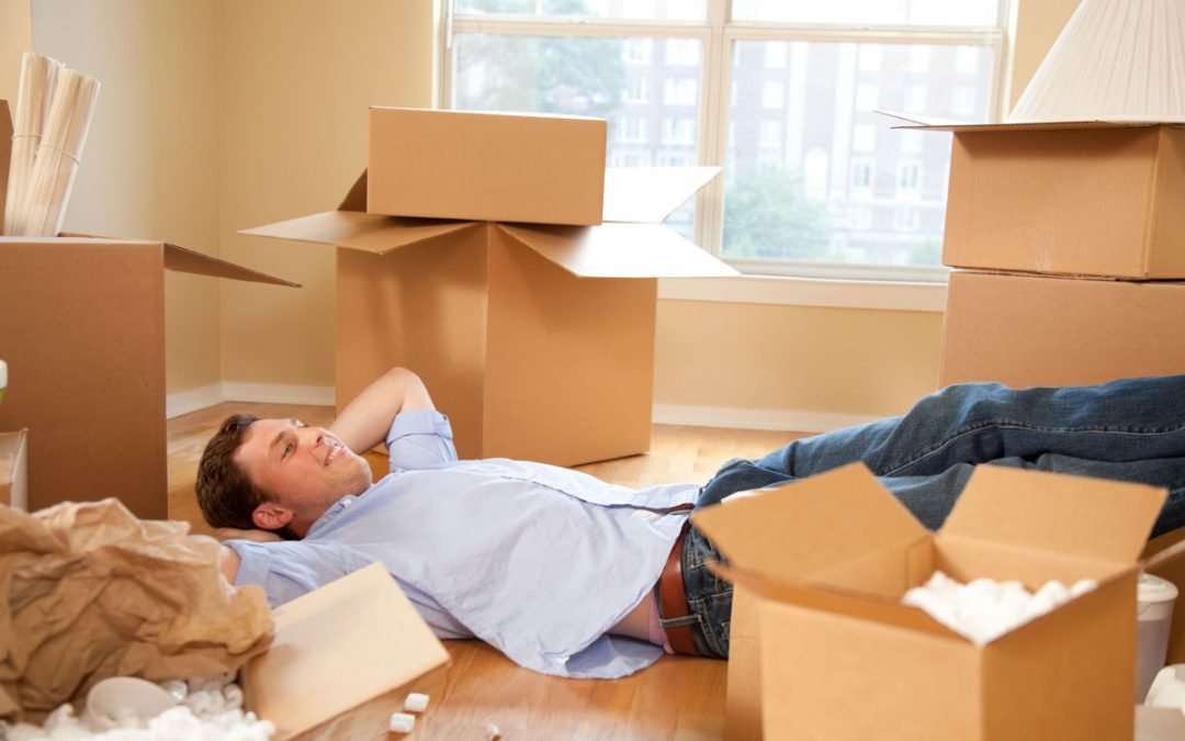 A happy man laying on the floor of his new flat surrounded by partially unpacked removals boxes