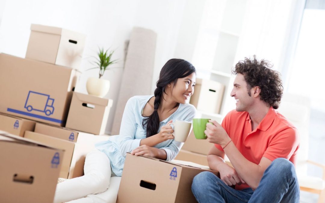 A happy couple sitting amongst removals boxes celebrating with mugs of coffee