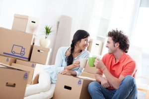 A happy couple sitting amongst removals boxes celebrating with mugs of coffee