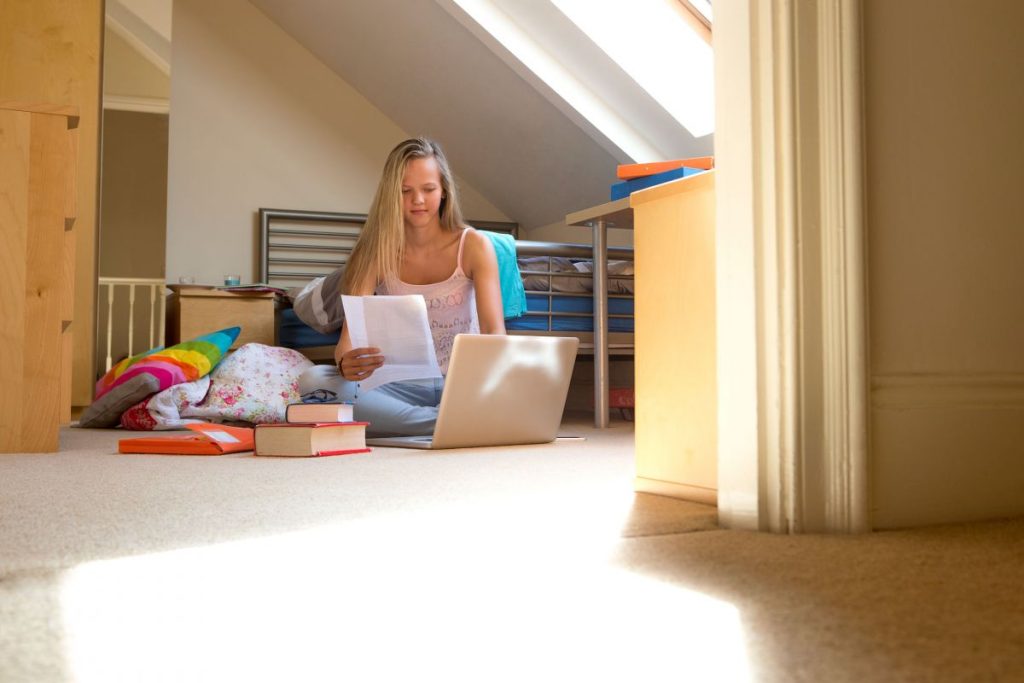 A student sitting on her bedroom floor with a laptop doing some homework