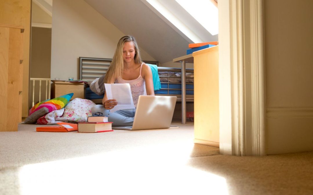A student sitting on her bedroom floor with a laptop doing some homework