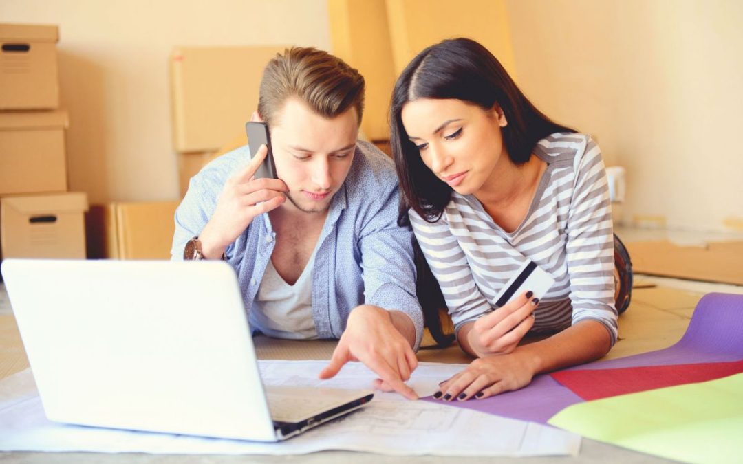 A couple laying on the floor researching on a laptop and speaking on a mobile phone