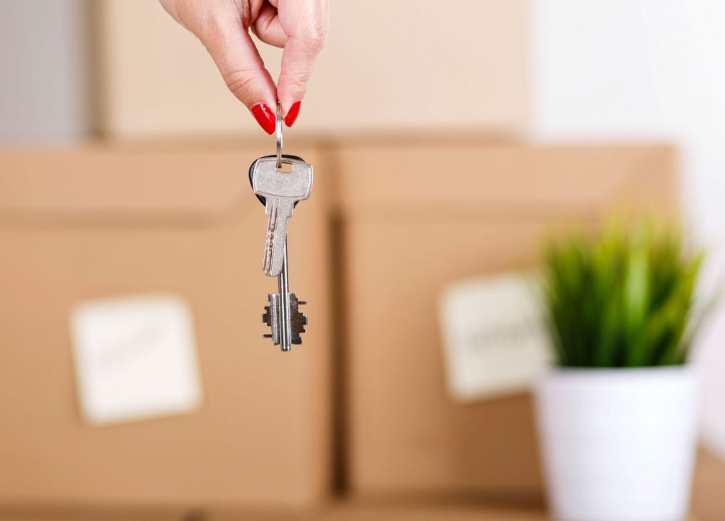 Keys to a new home being dangled in front of packed boxes and a house plant