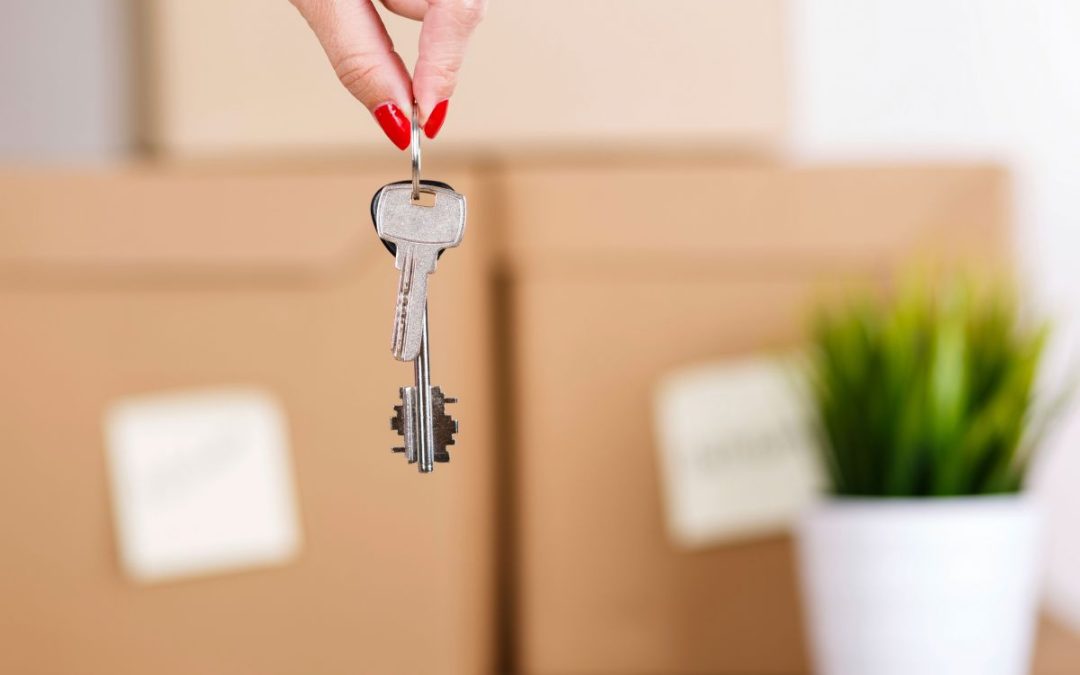 Keys to a new home being dangled in front of packed boxes and a house plant
