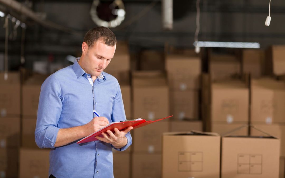 An employee ticking off inventory on a clipboard surrounded by belonging packed in cardboard boxes