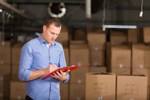 An employee ticking off inventory on a clipboard surrounded by belonging packed in cardboard boxes