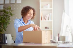 A young lady opening a cardboard box at her home office desk