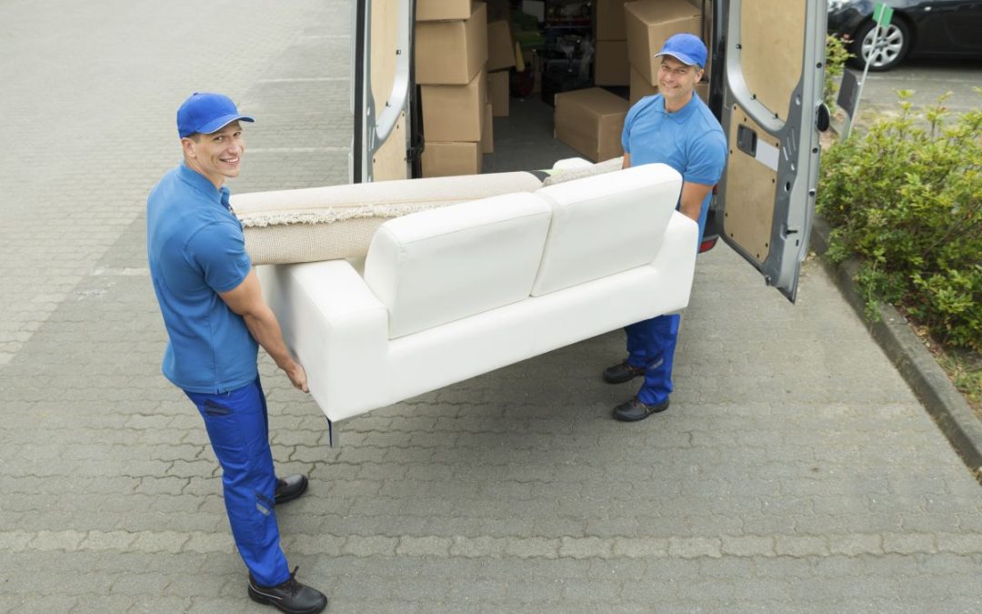 Two removals men unloading a sofa and rug from a delivery van filled with cardboard packing boxes