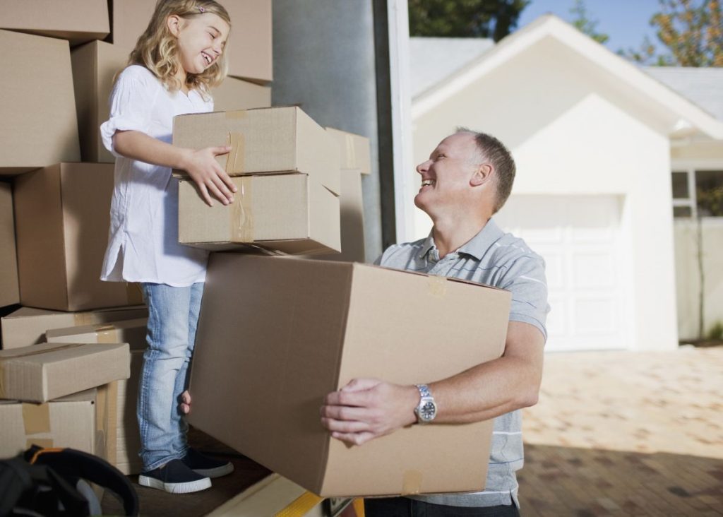A happy scene of a father and young daughter unloading boxes in front of their new home