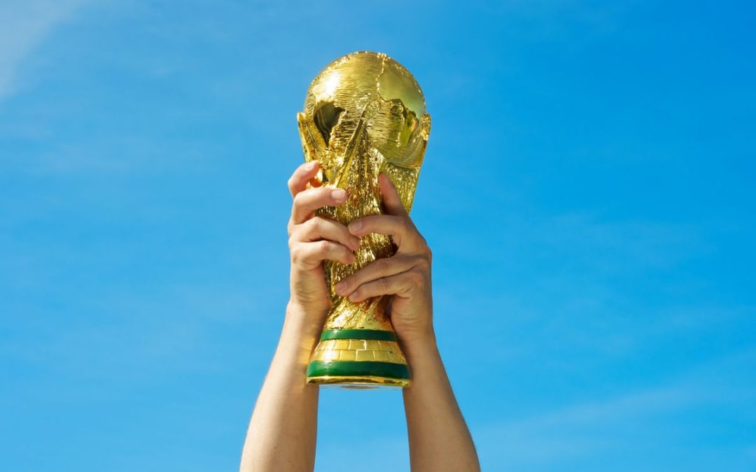 Hands holding the football World Cup aloft infront of a blue sky