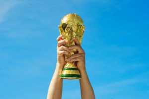 Hands holding the football World Cup aloft infront of a blue sky