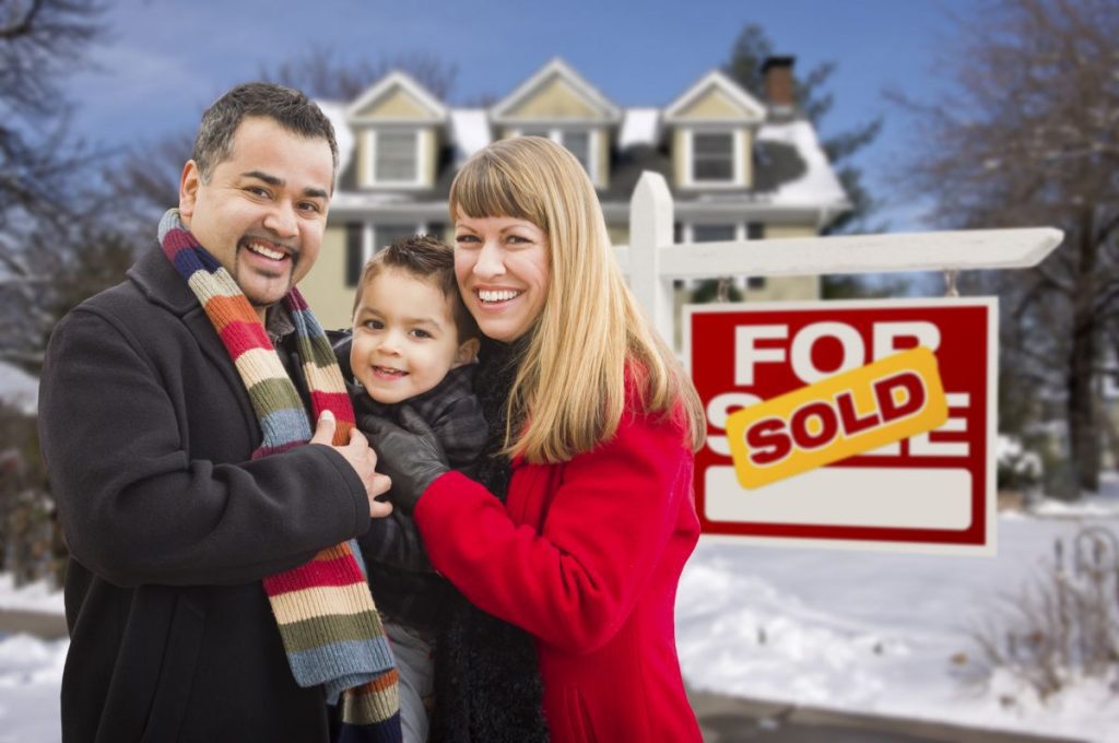 A happy looking mum, dad and son stood outside their new home with snow on the ground