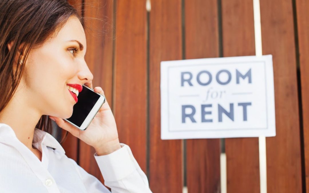 A young lady speaking on her mobile phone in front of a room for rent sign