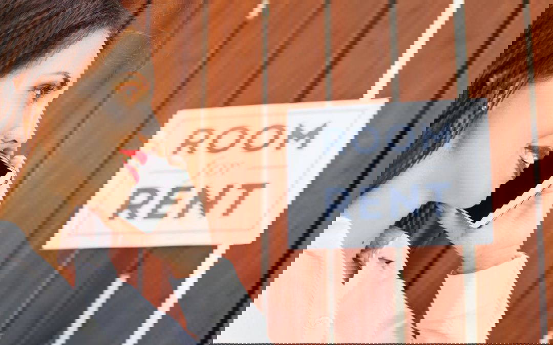 A young lady speaking on her mobile phone in front of a room for rent sign