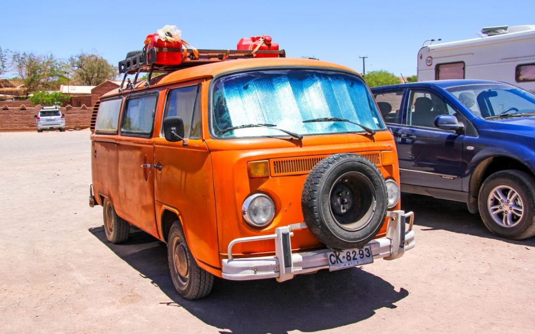 A vintage orange VW campervan parked in a car park with other vehicles