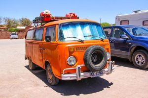 A vintage orange VW campervan parked in a car park with other vehicles