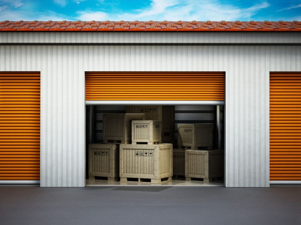 An external view of an open roller shutter door and crated belonging inside a storage room