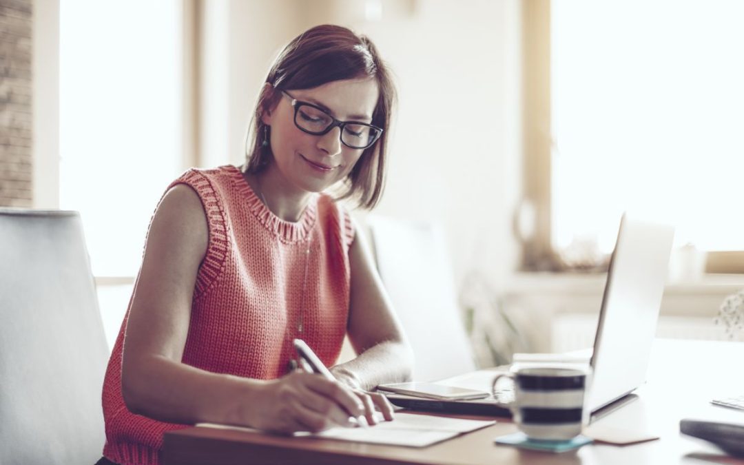 A woman writing notes in front of her computer sat at the dining table in her new home