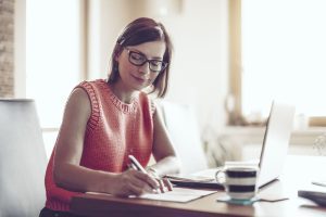 A woman writing notes in front of her computer sat at the dining table in her new home