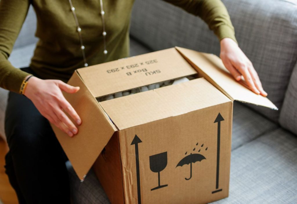 A lady sat on a sofa opening a cardboard packing box filled with personal belongings