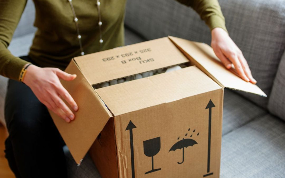 A lady sat on a sofa opening a cardboard packing box filled with personal belongings