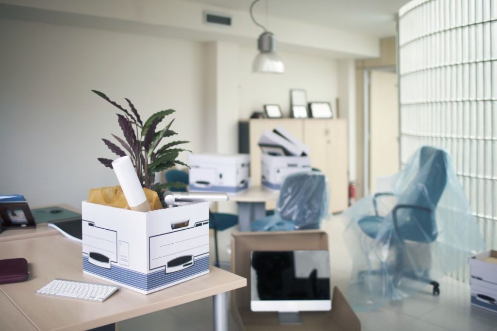 A modern office environment with cardboard boxes filled with stationery and Polythene covered chairs ready for moving