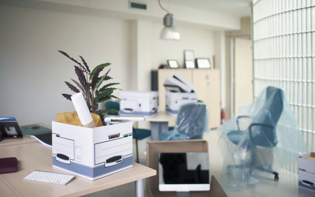A modern office environment with cardboard boxes filled with stationery and Polythene covered chairs ready for moving