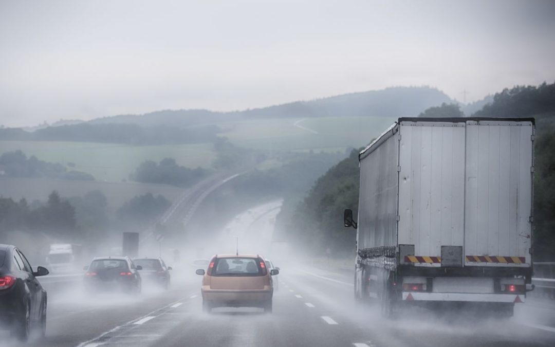 A busy motorway scene with rolling hills in heavy rain with lots of spray coming from lorries and cars