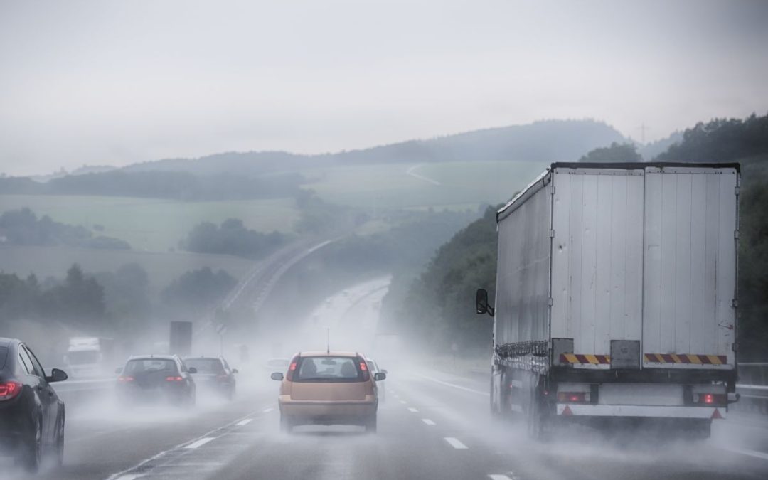 A busy motorway scene with rolling hills in heavy rain with lots of spray coming from lorries and cars