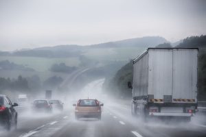 A busy motorway scene with rolling hills in heavy rain with lots of spray coming from lorries and cars