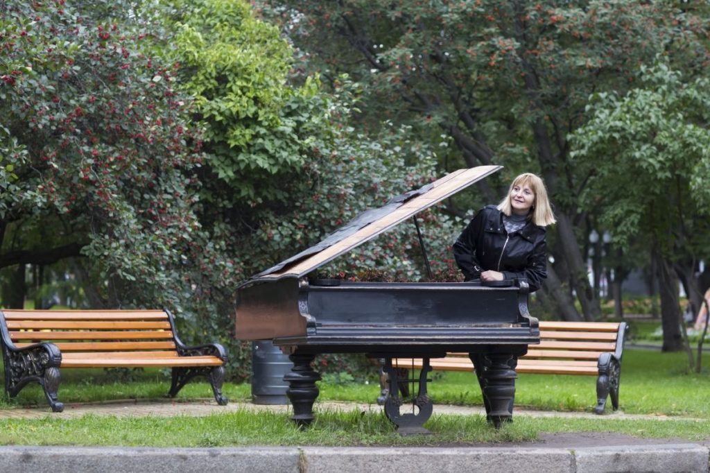 A lady in a public park leaning on a black grand piano