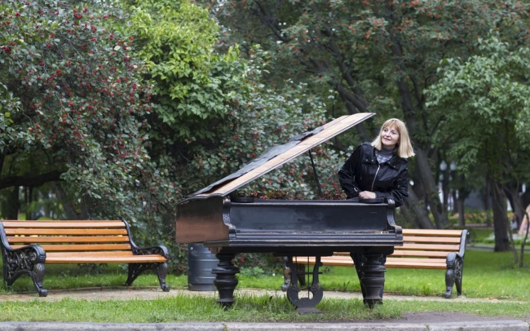 A lady in a public park leaning on a black grand piano