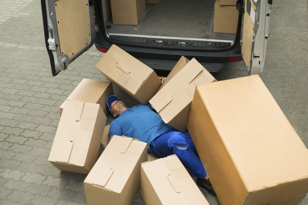 A delivery driver laying on the floor surrounded by cardboard boxes