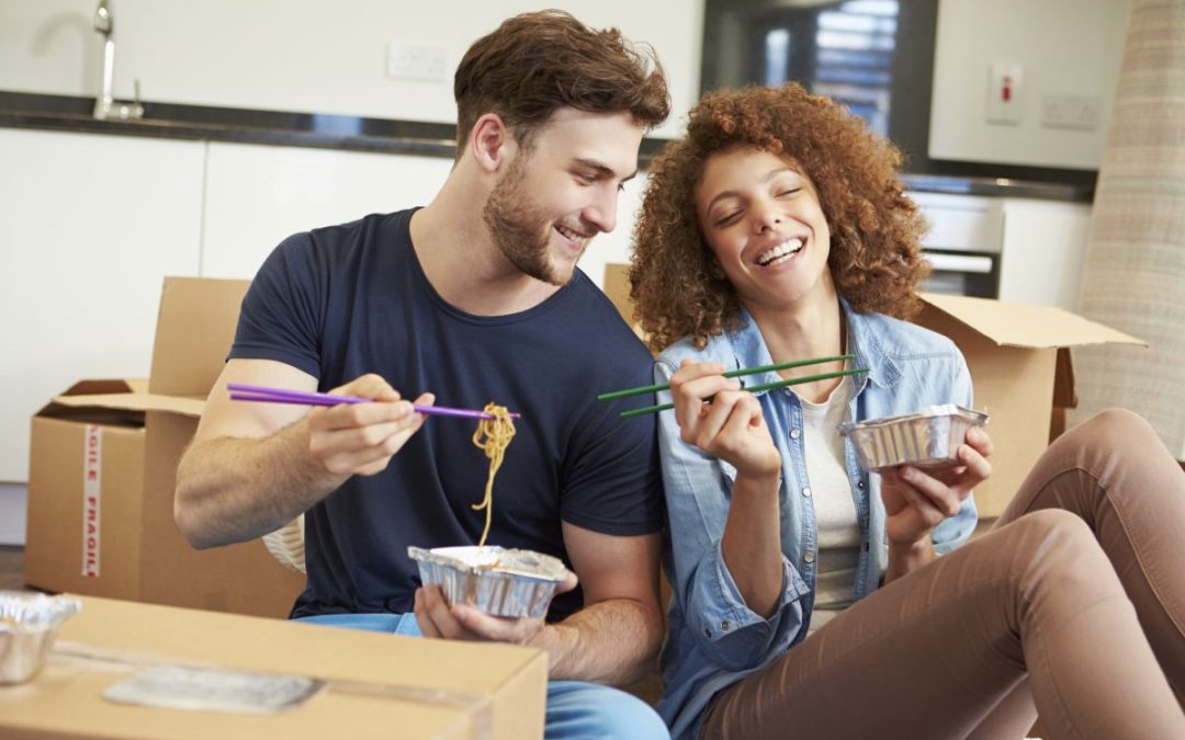 A happy young couple celebrating moving into their new house with a takeaway Chinese meal while surrounded by cardboard packing boxes