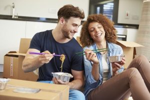 A happy young couple celebrating moving into their new house with a takeaway Chinese meal while surrounded by cardboard packing boxes