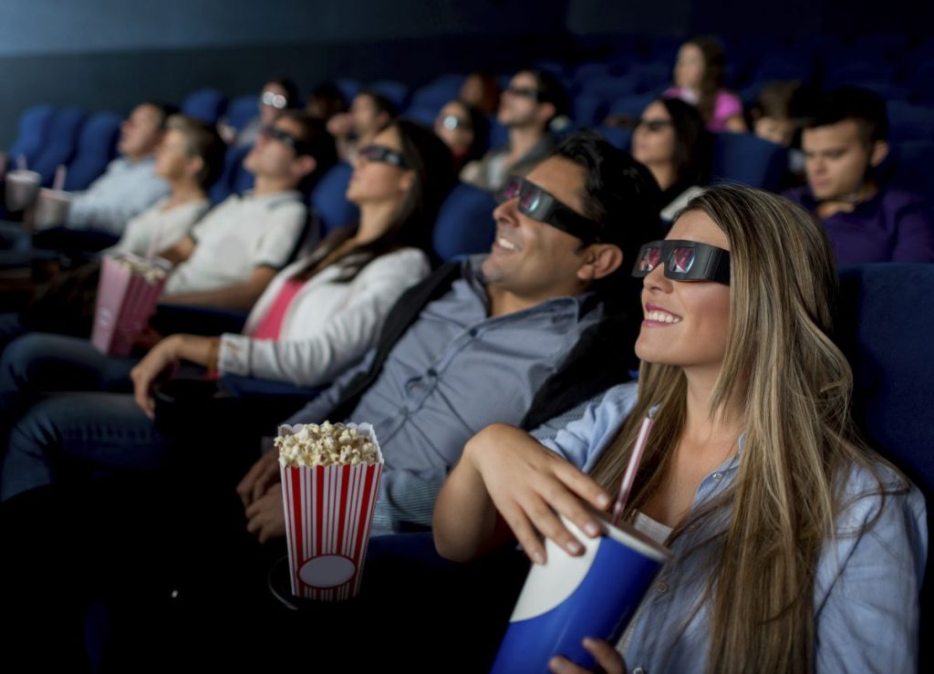 People sat in a cinema wearing 3D glasses enjoying a film with drinks and popcorn