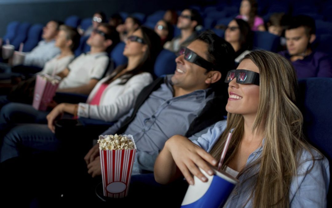 People sat in a cinema wearing 3D glasses enjoying a film with drinks and popcorn