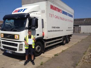 A removals lorry driver holding up his pass certificate in front of the driver training lorry