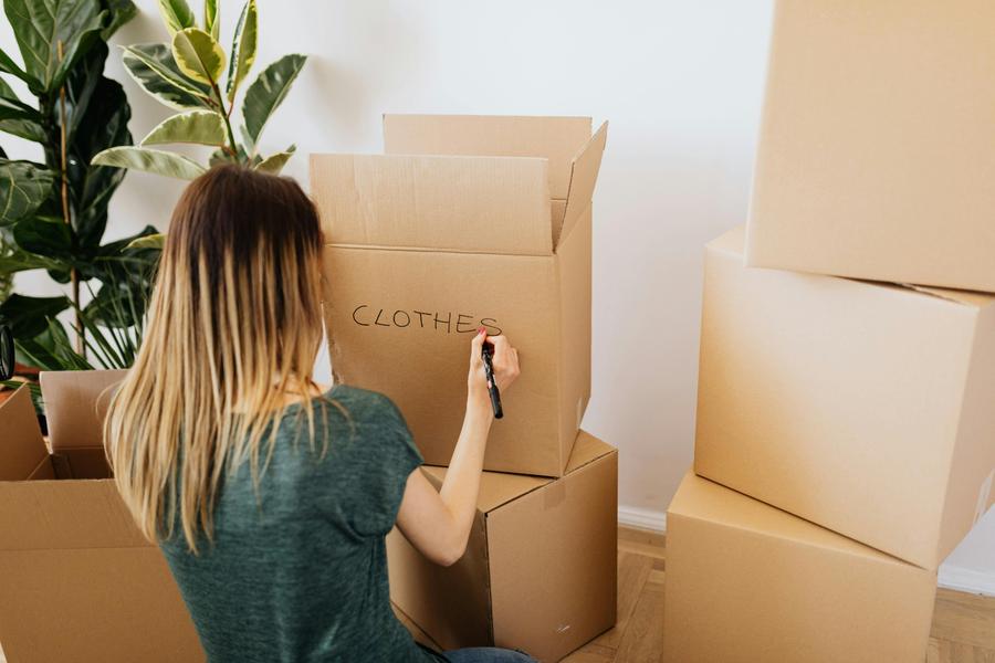 Woman labeling a cardboard box with the word "clothes".